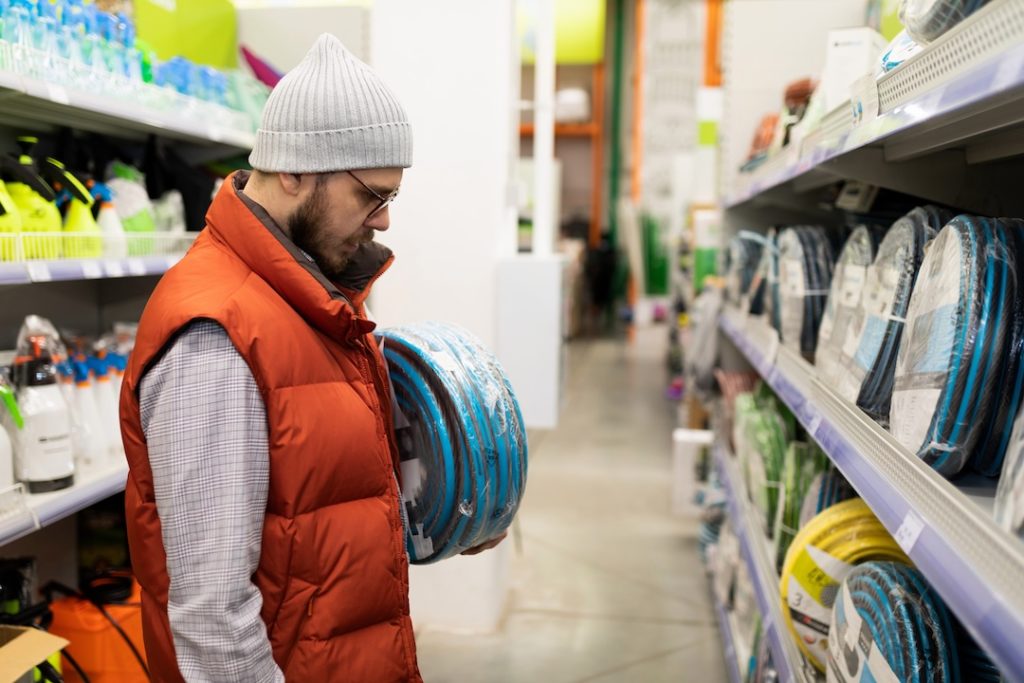 a customer in a garden supply store chooses a rubber watering hose.